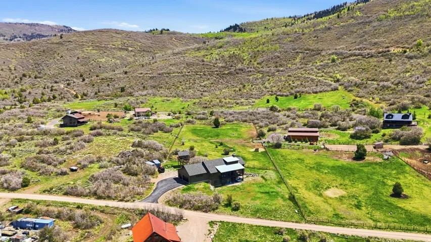 Expansive property featuring multiple structures, verdant green fields, natural brush, and mountainous terrain