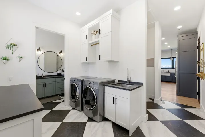 Dedicated laundry area featuring a checkerboard tile floor, built-in white cabinetry, a utility sink with a black countertop, and contemporary front-load appliances