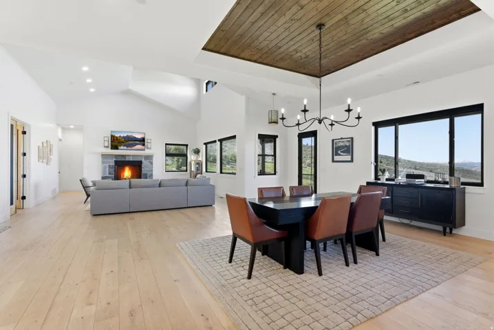 Spacious living area featuring light wood-finish flooring, a stone fireplace with a substantial mantel, and vaulted ceilings with recessed lighting