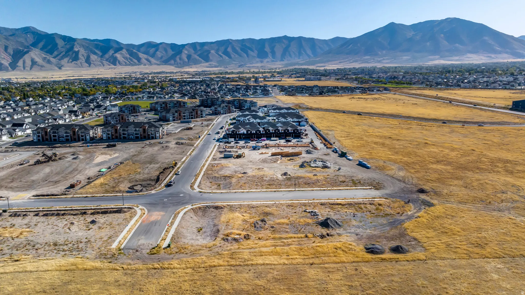 Expansive undeveloped land featuring paved street infrastructure and utility access, surrounded by residential developments and mountains