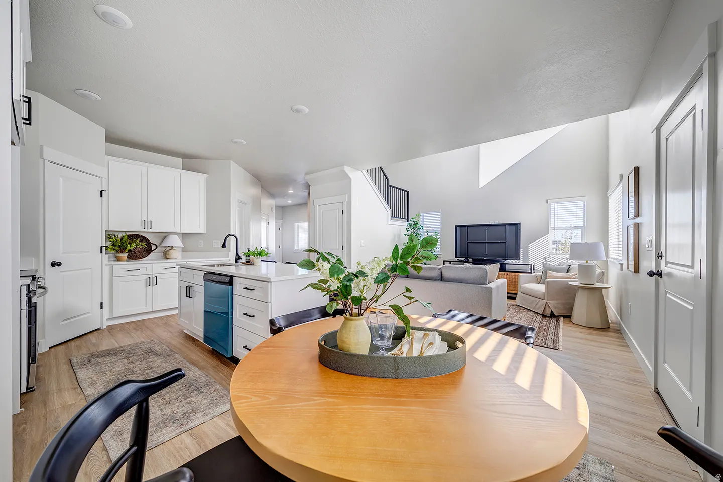 Open-concept living space featuring wood-finish flooring, white cabinetry, a kitchen island with seating, a stainless steel dishwasher, and recessed lighting