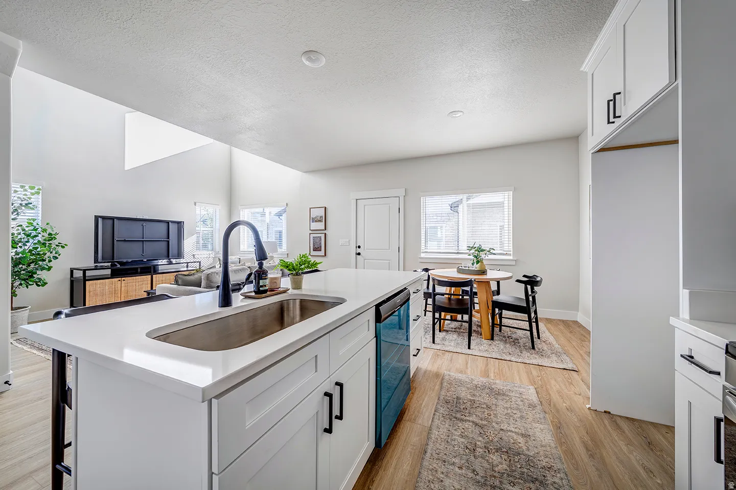 Modern kitchen featuring a white countertop island with an undermount sink and matte black faucet, integrated dishwasher, and white shaker cabinetry