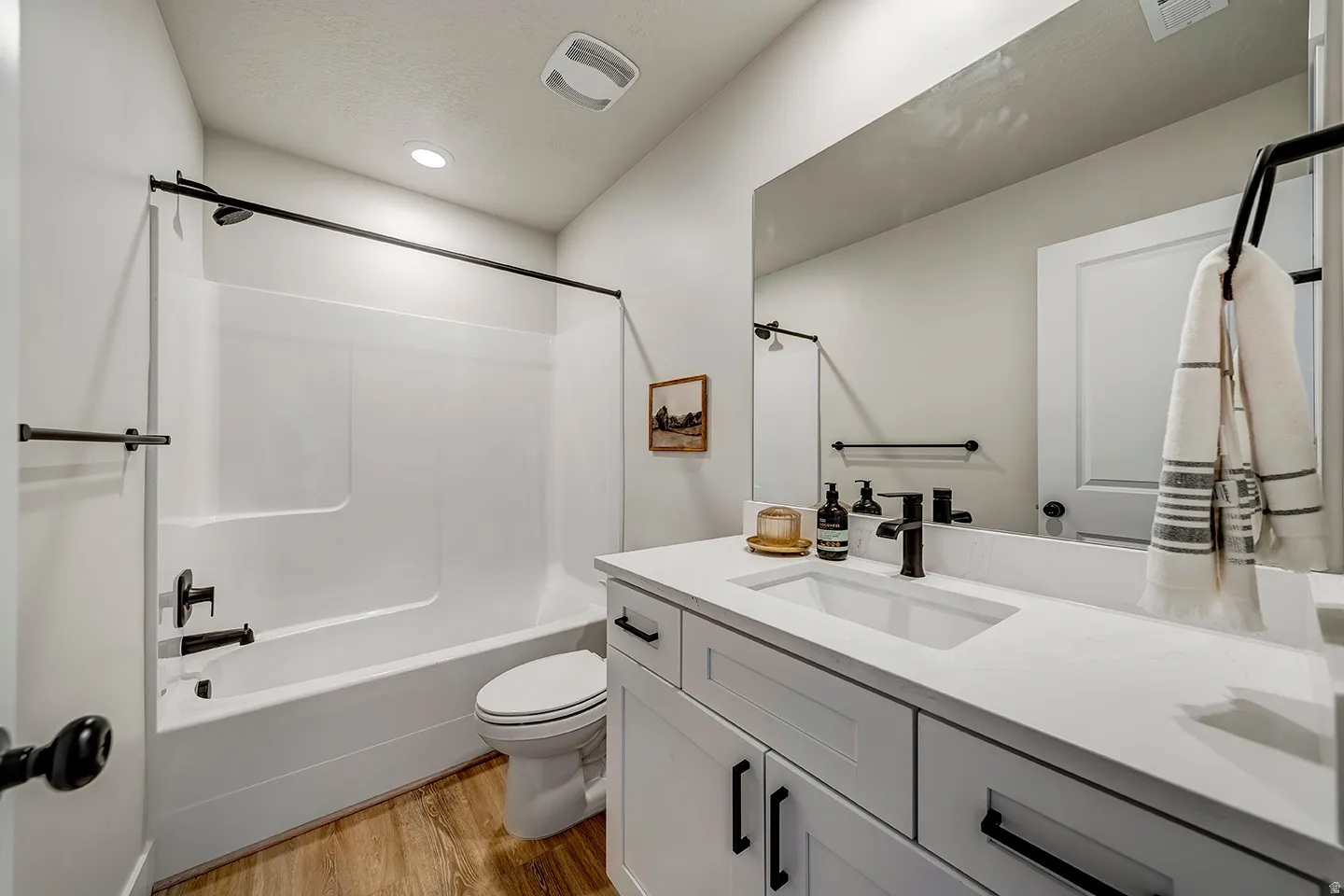 Modern bathroom featuring a white vanity with integrated sink, a white tub-shower combination, and wood-finish flooring
