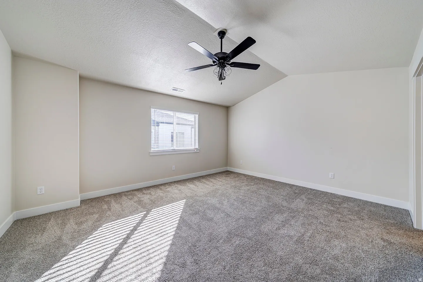 Spacious room featuring vaulted ceilings, a black ceiling fan, and light gray carpet
