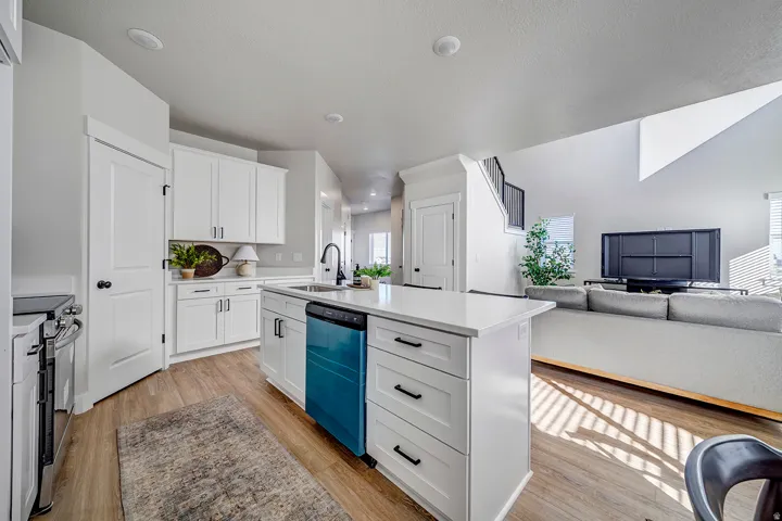 Open-concept living area featuring a kitchen island with built-in dishwasher, white cabinetry, wood-finish flooring, and recessed lighting