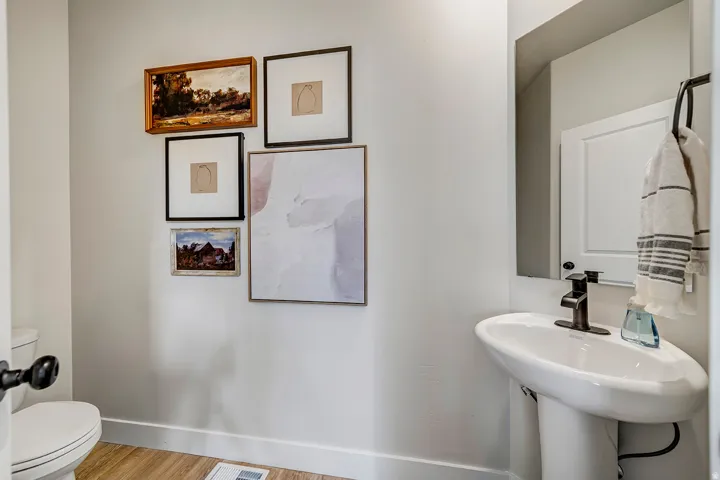 Pedestal sink with dark bronze faucet, framed mirror, and wood-finish flooring