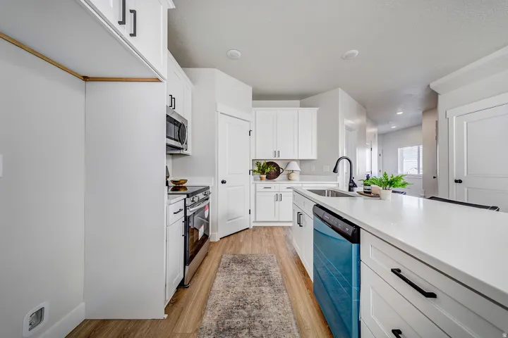 Modern kitchen featuring white shaker cabinetry, stainless steel appliances, a center island with countertop seating, a single basin sink with a gooseneck faucet, and wood-finish flooring