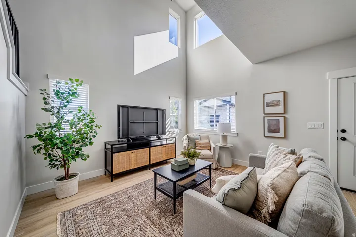 Living area featuring vaulted ceilings, high windows, wood-finish flooring, a white paneled door, and ample natural light