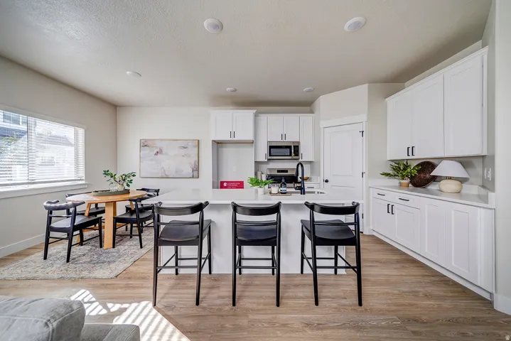 Open-concept kitchen featuring white cabinetry, a central island with countertop seating, stainless steel appliances, and wood-finish flooring
