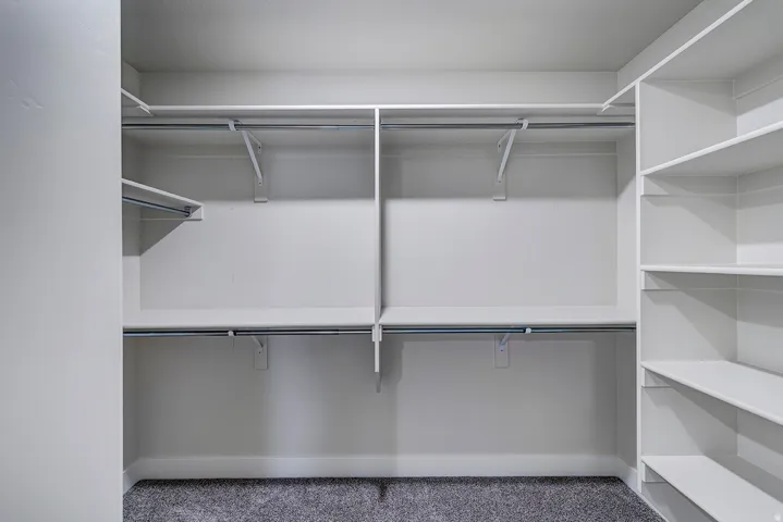 Walk-in closet with ample storage, featuring built-in shelving, multiple hanging rods, and a neutral carpeted floor