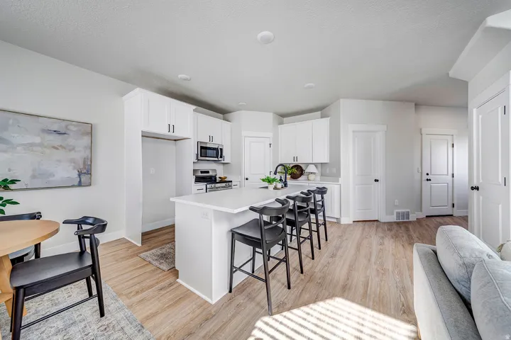 Modern kitchen featuring white cabinetry, a central island with countertop seating, stainless steel appliances, and light wood-finish flooring