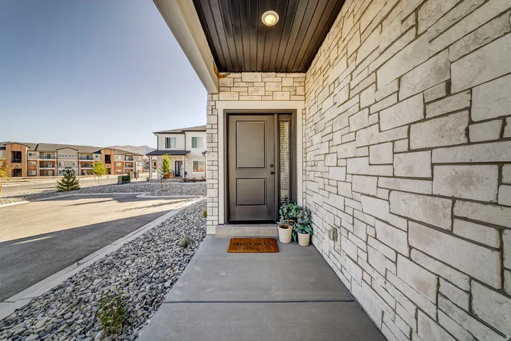 Front entry featuring a contemporary dark-paneled door, natural stone veneer siding, concrete walkway, and a dark wood soffit with recessed lighting