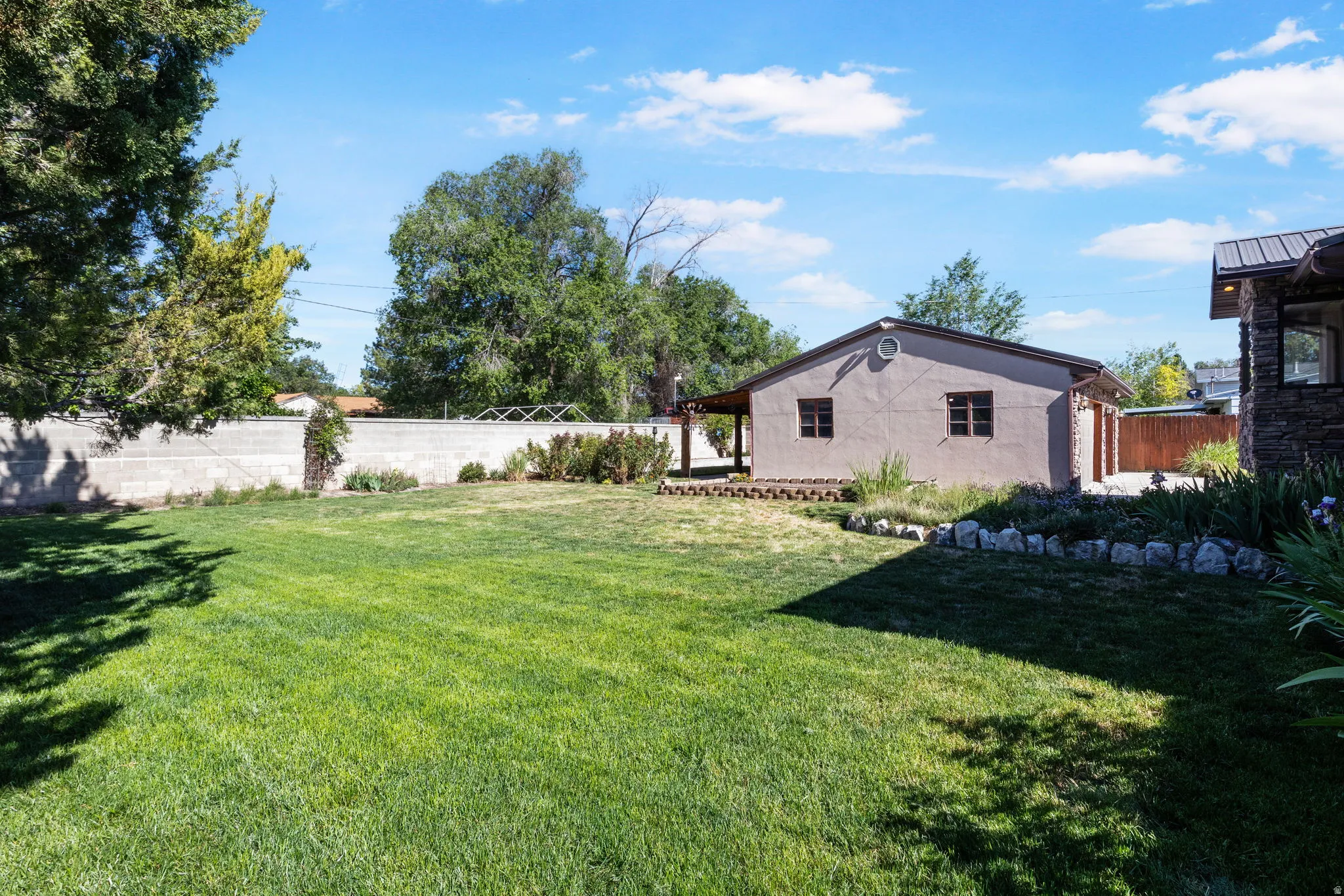 Backyard View #1-Expansive lawn with mature landscaping, a concrete block privacy wall and a covered patio.