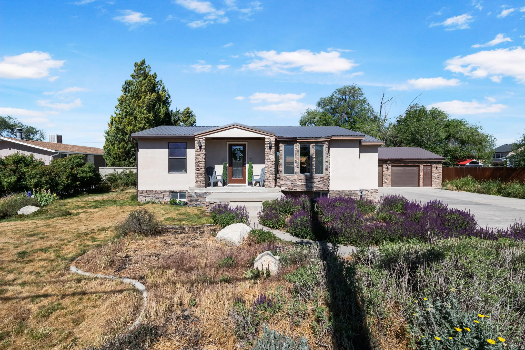 Stucco and stone facade home featuring a bay window, covered entry, and a multi-car driveway leading to a detached garage.