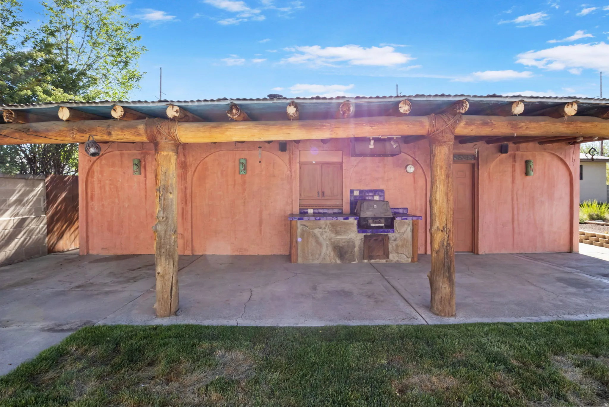 Covered patio featuring rustic wood pillars, a built-in grill, tile countertop, and stucco wall.