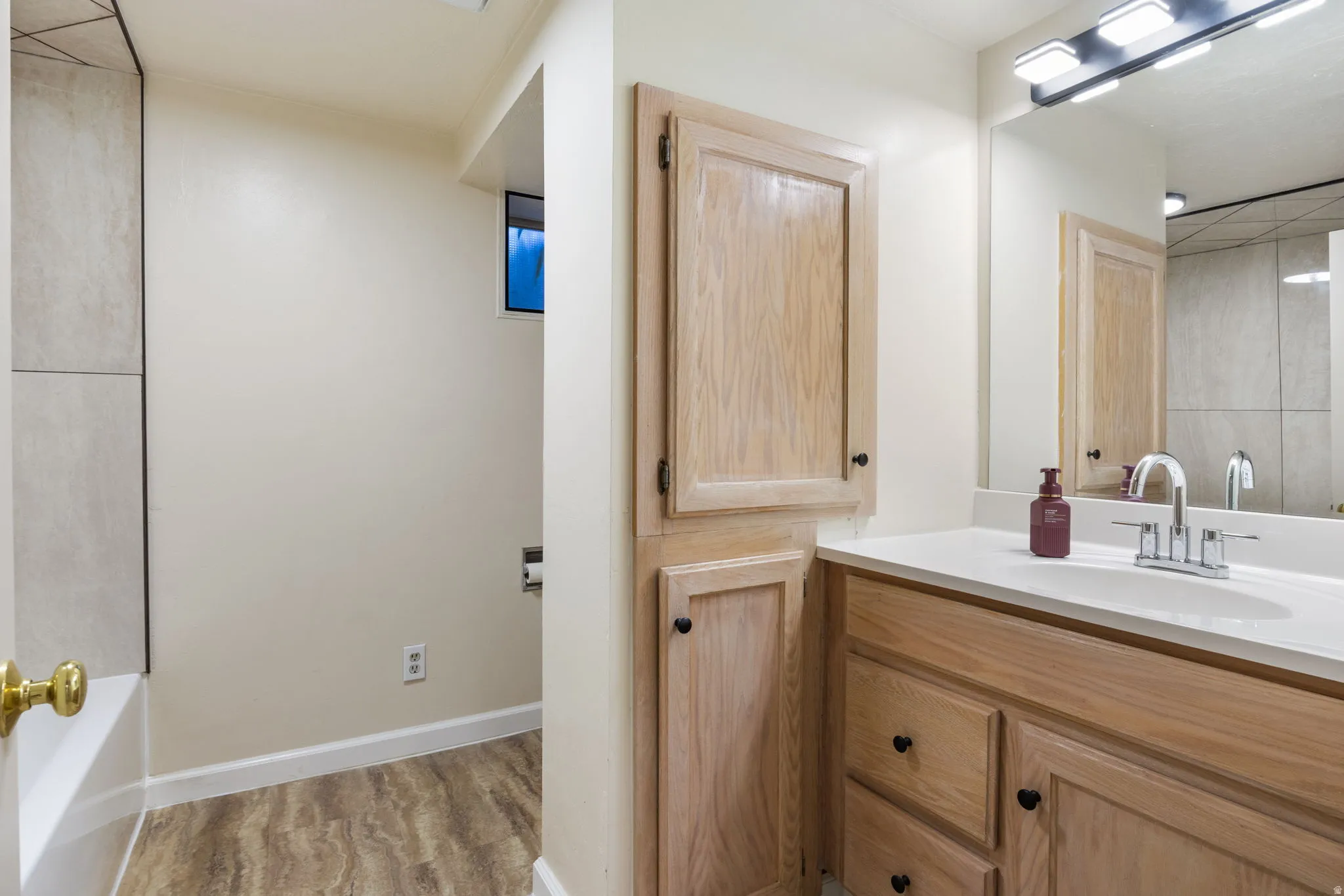 Bathroom vanity with light wood-finish cabinetry, a white countertop, and an integrated sink. Basement Bathroom-View #1.