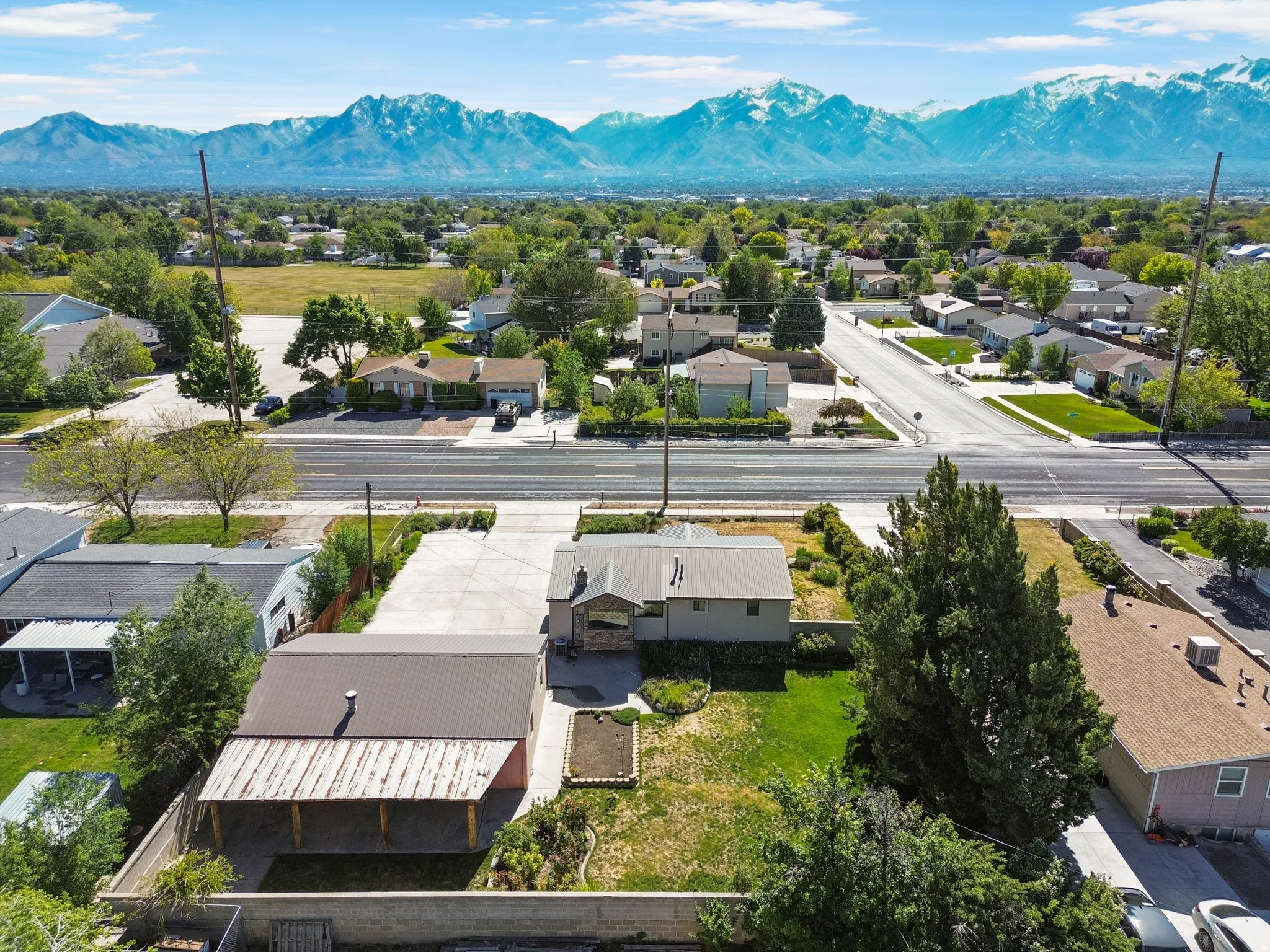 Expansive property featuring two structures with metal roofing, a large paved driveway, and mature landscaping. Aerial View #2.