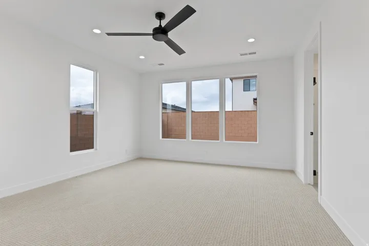 Spacious room featuring neutral carpeting, multiple windows, a modern ceiling fan, and recessed lighting