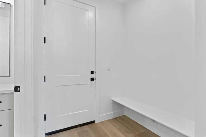 Entryway featuring a white paneled door with matte black hardware, wood-finish flooring, a built-in white bench, and a white vanity with a mirror