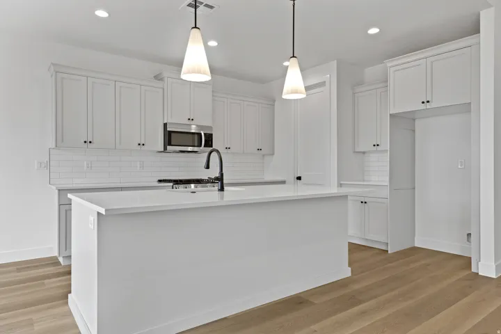 Kitchen featuring a large central island, white shaker cabinetry, stainless steel microwave, black faucet, and light wood-finish flooring