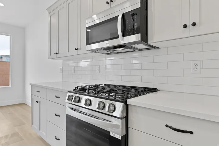 Contemporary kitchen featuring white shaker cabinetry, stainless steel oven/range with an overhead microwave, white subway tile backsplash, light-toned countertops, and wood-finish flooring