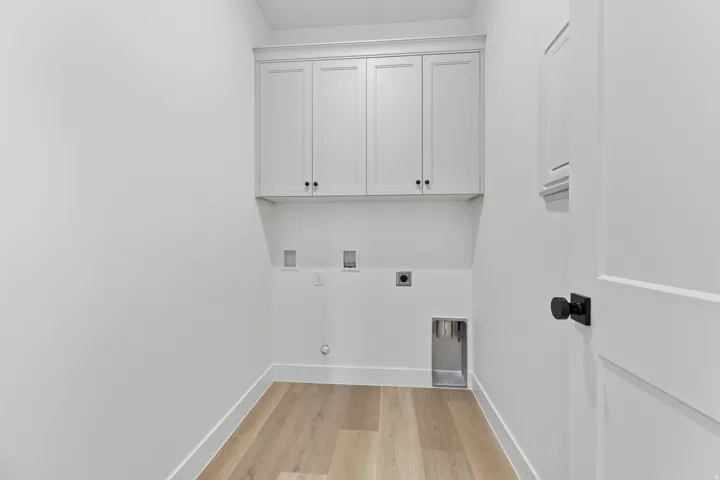 Dedicated utility space featuring light wood-finish flooring, white shaker-style cabinetry with black hardware, and a white interior door with a black knob