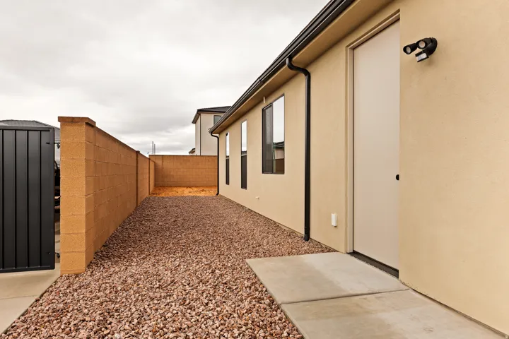 Side yard featuring a concrete block privacy wall, gravel ground cover, and a concrete pathway to an exterior door