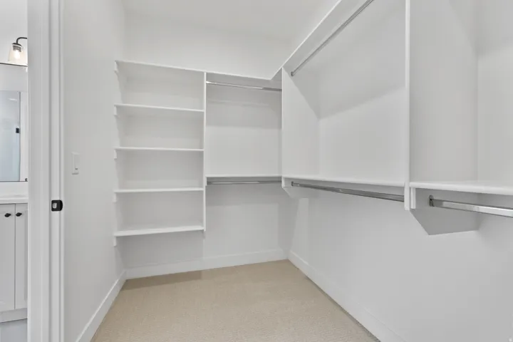 Walk-in closet featuring white built-in shelving, multiple hanging rods, and light-colored carpet flooring