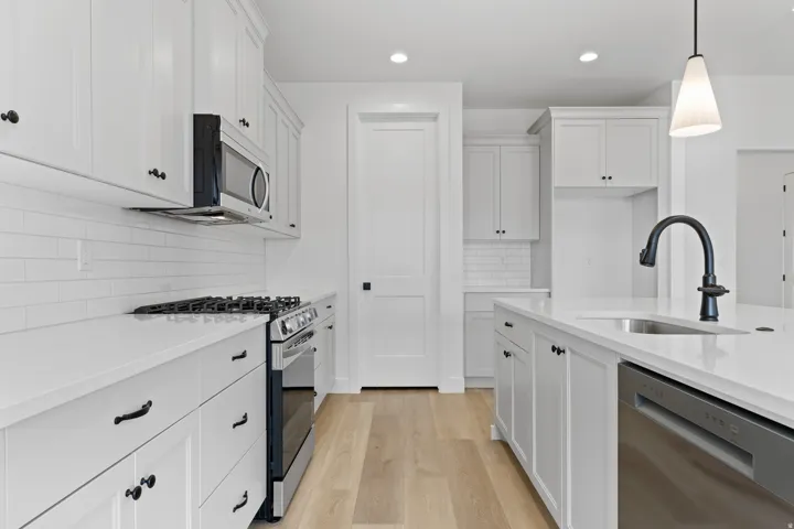 Contemporary kitchen with white cabinetry, stainless steel appliances, light wood-finish flooring, white subway tile backsplash, and a central island featuring a stainless steel sink and matte black faucet