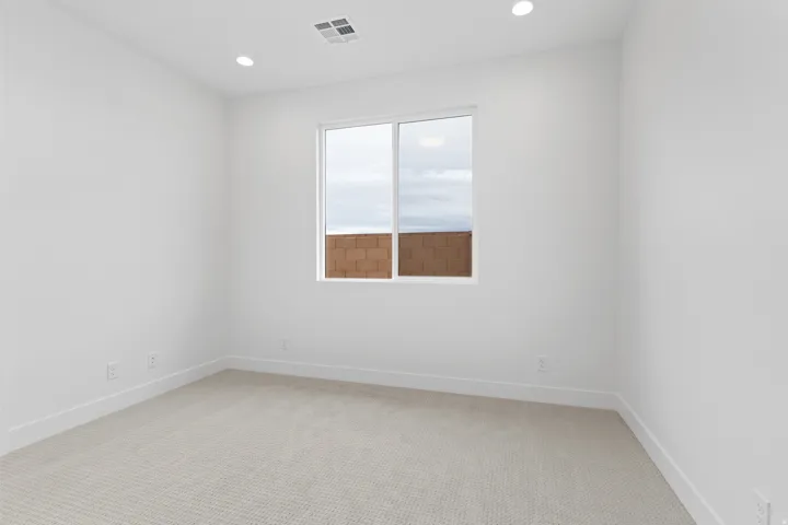 Bright interior space featuring a window with a white frame, light-colored carpet, recessed ceiling lighting, and white baseboards