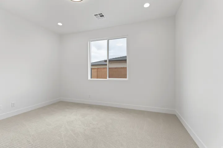 Bright room featuring a window with white trim, light-colored carpeting, white walls, recessed ceiling lighting, and a central ceiling light fixture