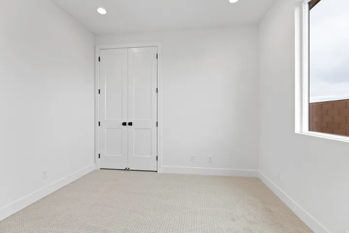 Bedroom featuring neutral wall-to-wall carpeting, white walls, and a prominent window with a white frame