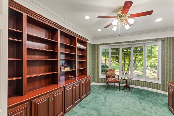 Living area with wallpapered walls, dark colored carpet, a ceiling fan, and crown molding