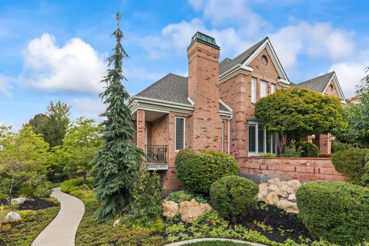 View of front of house featuring brick siding, a shingled roof, a balcony, and a chimney