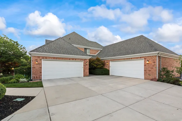 Traditional-style home featuring a shingled roof, brick siding, a garage, and driveway