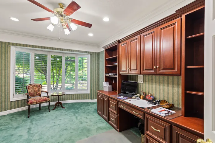 Office space featuring wallpapered walls, built in study area, light carpet, ceiling fan, and ornamental molding