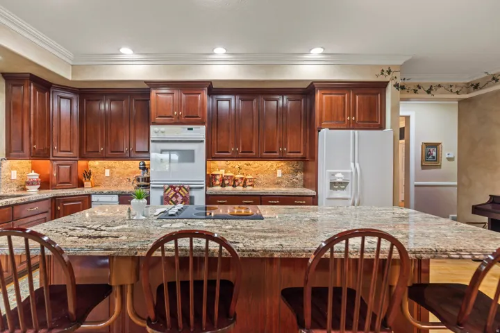 Kitchen with white appliances, light stone counters, a breakfast bar area, ornamental molding, and recessed lighting