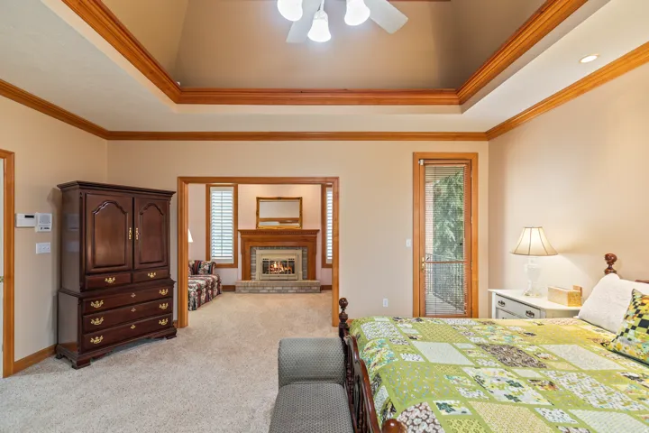 Bedroom with a tray ceiling, access to outside, ornamental molding, a fireplace, and multiple windows