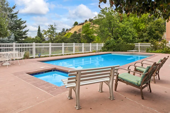 View of pool featuring patio surround, view of wooded area, and an in-ground hot tub