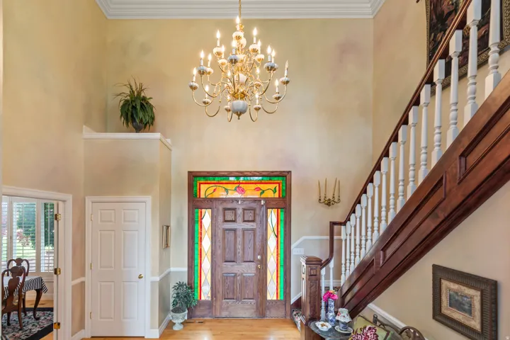 Entryway with hanging lights, a high ceiling, crown molding, and light wood-style floors