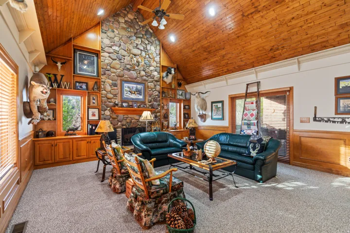 Living area with wainscoting, wood walls, a high wooden ceiling, carpet flooring, and ceiling fan