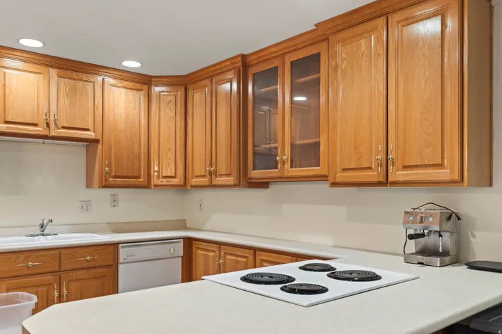 Kitchen featuring glass fronted cabinets, light countertops, wood finish cabinetry, recessed lighting, and dishwasher