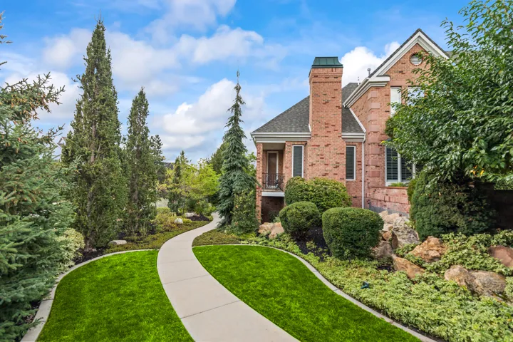 View of front of home with brick siding, a front lawn, a balcony, a chimney, and roof with shingles