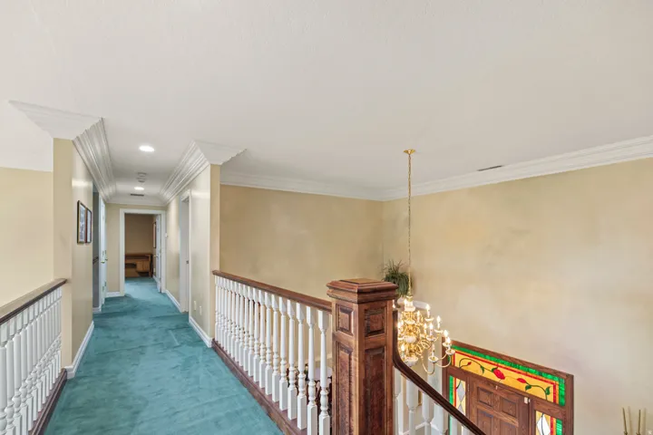 Corridor with suspended lighting, carpet flooring, ornamental molding, and an upstairs landing