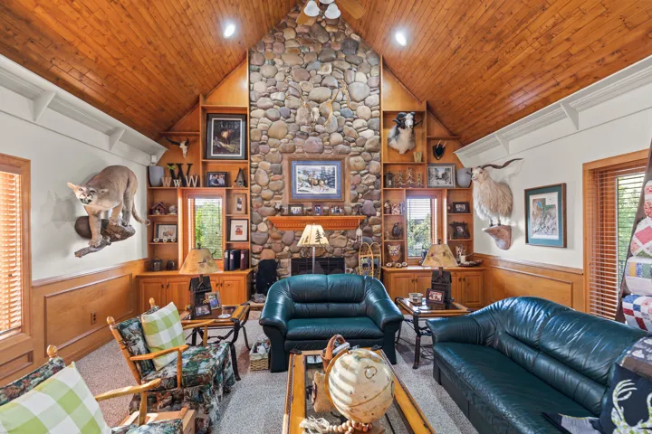 Living area with a wainscoted wall, plenty of natural light, a stone fireplace, a decorative wall, and ceiling fan