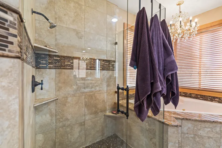 Full bath featuring a shower stall, suspended lighting, a tub with jets, and a towel warming rack