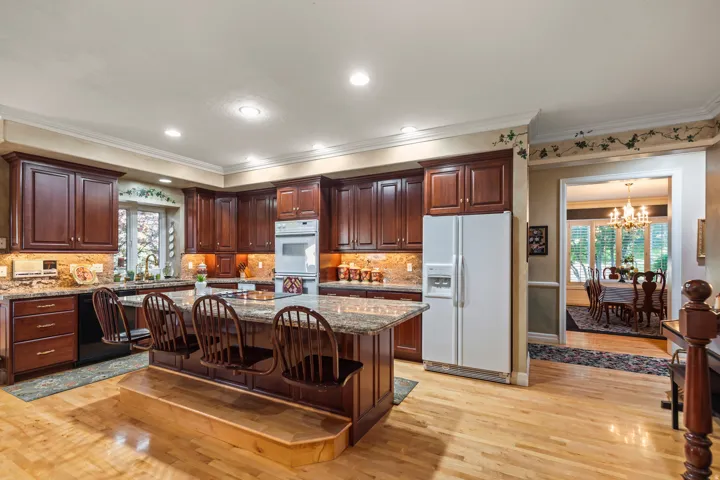 Kitchen with white appliances, light stone counters, a kitchen island, a kitchen bar, and dark wood finish cabinetry