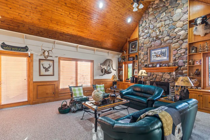 Carpeted living room with a wainscoted wall, a vaulted wooden ceiling, a decorative wall, a fireplace, and a ceiling fan