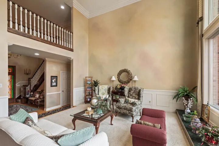 Carpeted living room featuring crown molding, a decorative wall, a high ceiling, a wainscoted wall, and recessed lighting