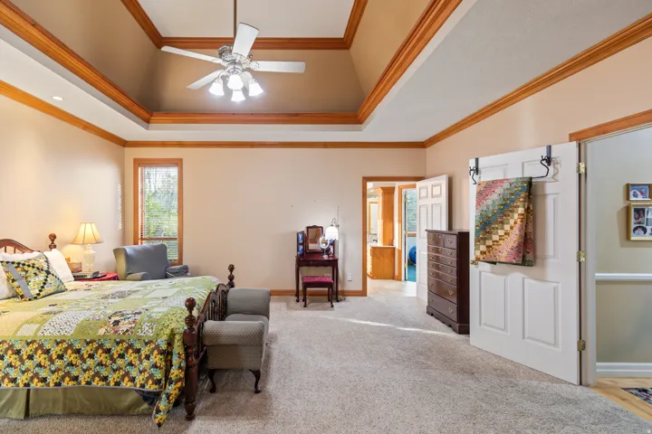 Carpeted bedroom featuring a ceiling fan, ornamental molding, and a raised ceiling
